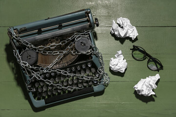 Vintage typewriter with chains, eyeglasses and crumpled paper on green wooden background. Printing...