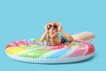 Cute little boy lying on swim mattress against blue background