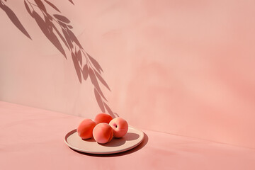 A modern still life featuring peaches on a beige plate, with a botanical shadow cast onto a textured pink wall. A warm color palette has been employed.