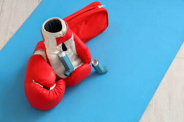Asthma inhalers with boxing gloves and first aid kit on mat in gym, closeup