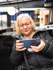 Defocused blonde gamer grandmother enjoying playing on smartphone - 780151541