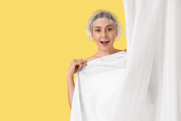 Young woman in shower cap with bathroom curtain on yellow background