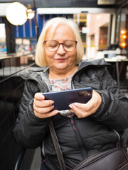 Defocused blonde gamer grandmother very concentrated playing on smartphone - 780151765