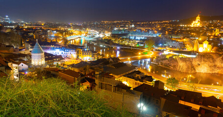 Scenic cityscape of town Tbilisi with illuminated buildings and bridges over Kura river, Georgia - obrazy, fototapety, plakaty