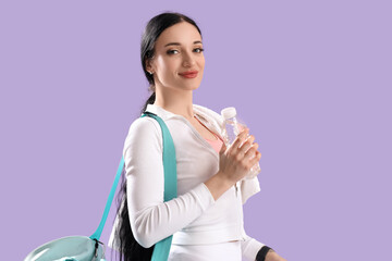 Portrait of sporty young woman with bottle of water and sport bag on lilac background
