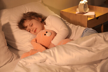 Adorable little girl with plush bunny sleeping in bed