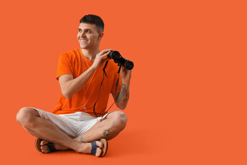 Male lifeguard with binoculars sitting on orange background
