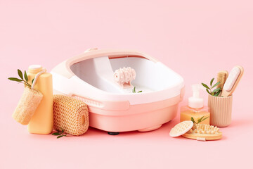 Massage foot bath, cosmetic products and sponges on pink background