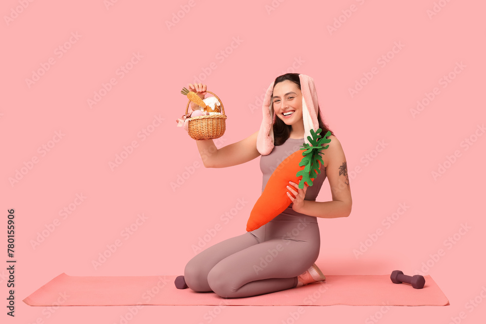 Sticker happy female fitness coach in bunny ears with easter basket, toy carrot and dumbbells on pink backgr