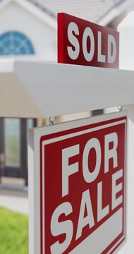 Vertical Pan of A Sold For Sale Real Estate Sign with a New Home in the Background.
