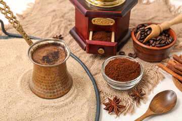 Pot of hot coffee in sand, beans and star anise on white background