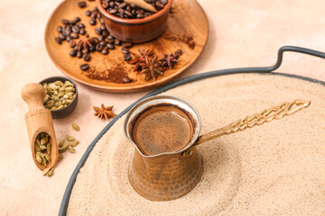 Pot of hot coffee in sand, wooden plate with coffee beans and star anise on light background