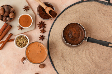 Pot of hot coffee in sand and different spices on light background