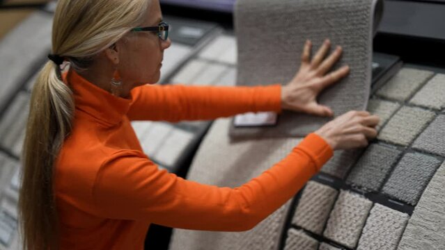 Closeup of mature womans hand moving across carpet or rug samples in a hardware store.