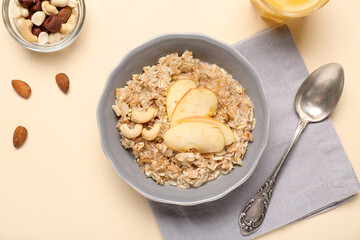 Tasty oatmeal with apple and cashew in bowl on beige background