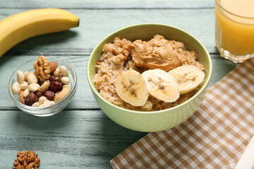 Bowl with tasty oatmeal, banana, peanut butter and nuts on wooden background
