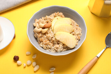 Tasty oatmeal with sliced apple and nuts on yellow background