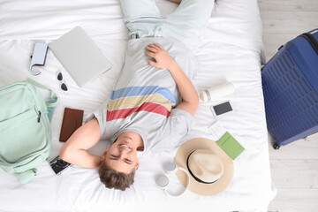 Male tourist with travel accessories lying on bed in hotel room, top view - obrazy, fototapety, plakaty