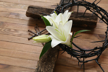 Crown of thorns with white lilies, nails and cross on wooden background