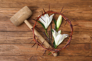 Crown of thorns, lilies, nails and hammer on wooden background