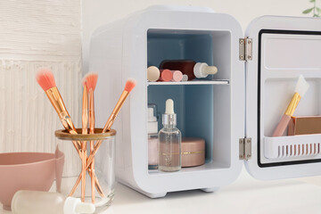 Open cosmetic refrigerator with products on chest of drawers near white wall