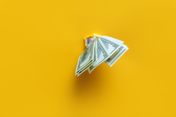 Hundred dollar bills poke out of a ragged hole in the yellow paper. Concept of income, salary,...