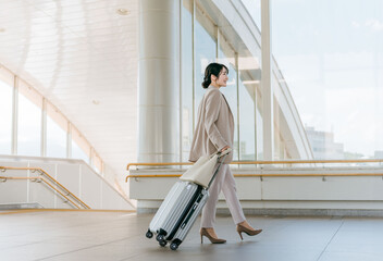 空港・駅・ビル・公共交通施設でスーツケースを持って歩くビジネスウーマン（海外出張・徒歩）
