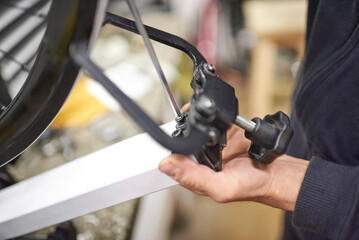 Maintenance service in a bicycle workshop: unrecognizable person aligning a bike wheel using a...