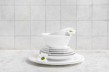Beautiful tableware with chamomiles on grunge table near white tile wall