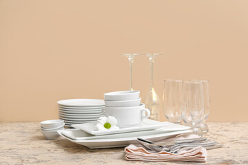 Composition with clean dishes, chamomile, glasses and cutlery on table near beige wall
