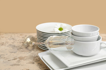 Composition with clean dishes, chamomile and glass on table near brown wall