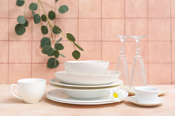 Beautiful tableware and leaves on table near orange tile wall
