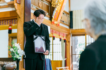 お葬式で遺影を持って挨拶する喪主の日本人男性（喪主の挨拶）
