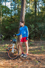 Youth cyclist standing against a tree with his mountain bike and riding gear