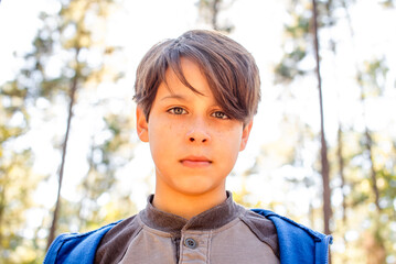 Close up head and shoulders portrait of a boy standing outdoors looking into the camera