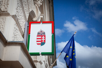 Hungarian coat of arms in front of a flag of European Union waiving in the Hungarian city of Pecs. Hungary is a member of the EU since 2004 and a major actor of the European game.