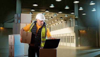 A warehouse employee checks boxes and parcels. A man in a reflective vest works in a warehouse.
