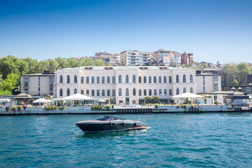 Panorama of the coast of Bosporus in Istanbul, turkey, with a small yacht posing in front of a luxury ottoman palace on the sea, in summer.