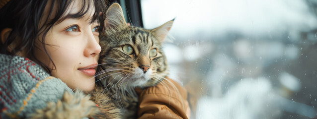 A woman and her cat gaze out a snowy window, reflecting a quiet bond between pet and owner in a cozy indoor setting.