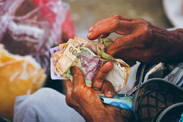 Older hands counting weathered paper Indonesian currency called Indonesian Rupiah, suggesting a...