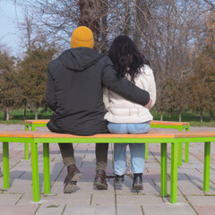 A couple in love hugs on a bench. Girl and guy in winter clothes sitting in the park, romantic date, happy lovers - 780211598