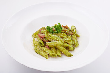 Penne pesto sauce with ham and bacon top with basil leaves served on white plate isolated on white background.