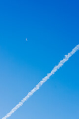 Cielo despejado con la luna en cuarto menguante y una estela de nube humo o vapor