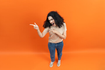 Excited Young Woman Pointing And Looking Surprised On Orange Background