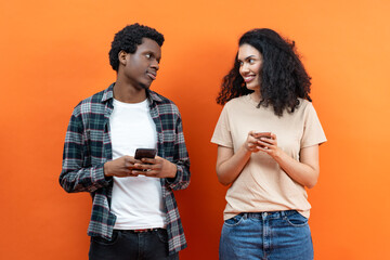 Young African American Man and Mixed Race Woman Using Smartphones on Orange Background, Social Media, Technology, Wireless Communication, Millennial Lifestyle, Connection, Diverse People