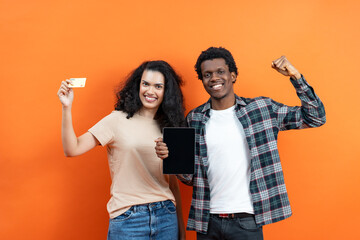 Happy Young Couple Celebrating Success With Tablet And Credit Card On Orange Background - Excited,...