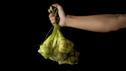 Hand presenting a ketupat pouch, a traditional Indonesian dish, woven from young coconut leaves...