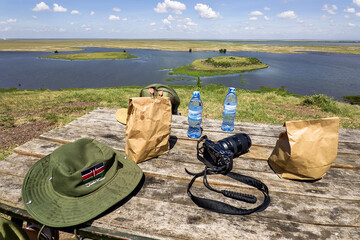 Food, water, hat, camera on the table against the background of nature. Wooden picnic table and...
