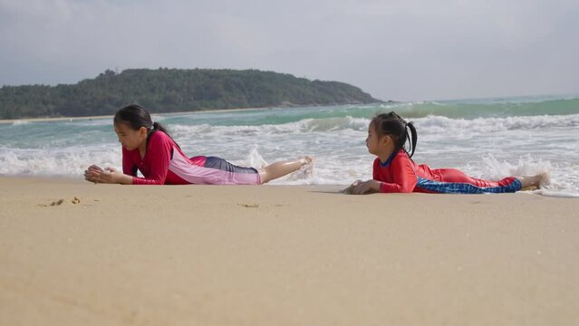 two happy asian kids lying on the beach playing with wave at riyue bay Wanning Hainan China