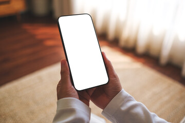 Mockup image of a woman holding mobile phone with blank desktop white screen at home